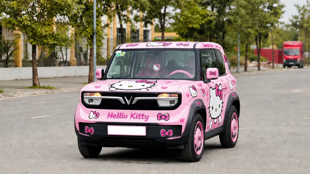 Vẫn chiếc xe đó sau khi AI sơn hồng bóng và dán kín sticker Hello Kitty, giữ nguyên dáng xe, góc chụp và khung cảnh phía sau